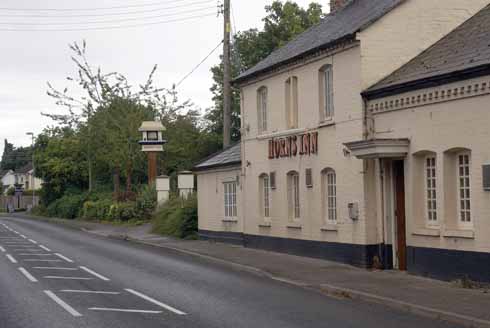 The main entrance of the Horns Inn had moved to the extension building to the right. Although the pub no longer has an Inn sign hanging over the road – which wouldn’t be terribly lorry-friendly – the upright for the cantilevered wrought iron sign support is still in place. The original sign bears the then publican’s name, Albert Cutler, on a plaque visible in the older picture