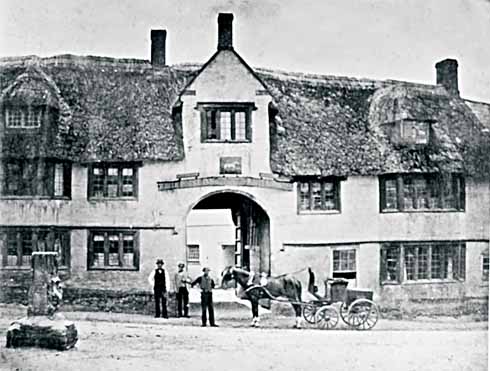 The White Horse at Maiden Newton, with the stub of the market cross at the left. When this photograph was taken – probably in the 1870s, but possibly the 1860s – it was still a super building with its original stone windows, and still thatched. 