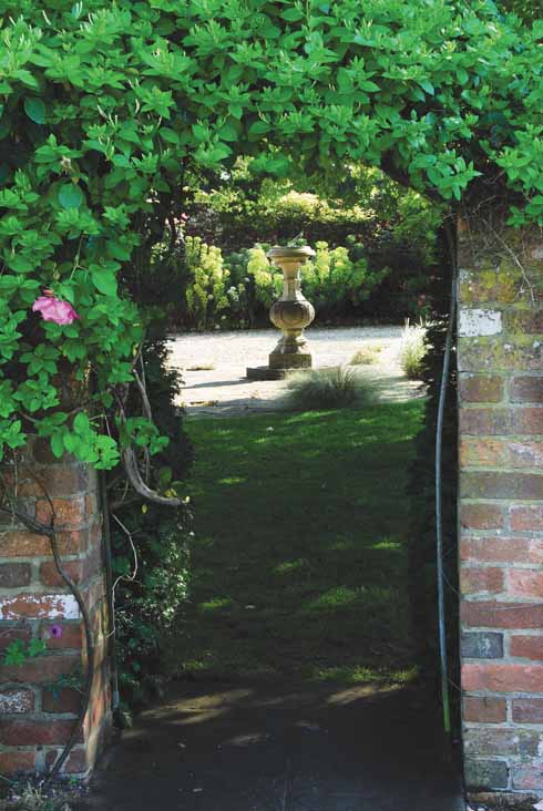 A sundial framed by a rose and honeysuckle-covered arch
